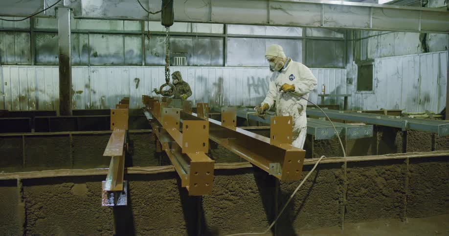 Two people use a spray paint gun to add paint to metal pieces indoors