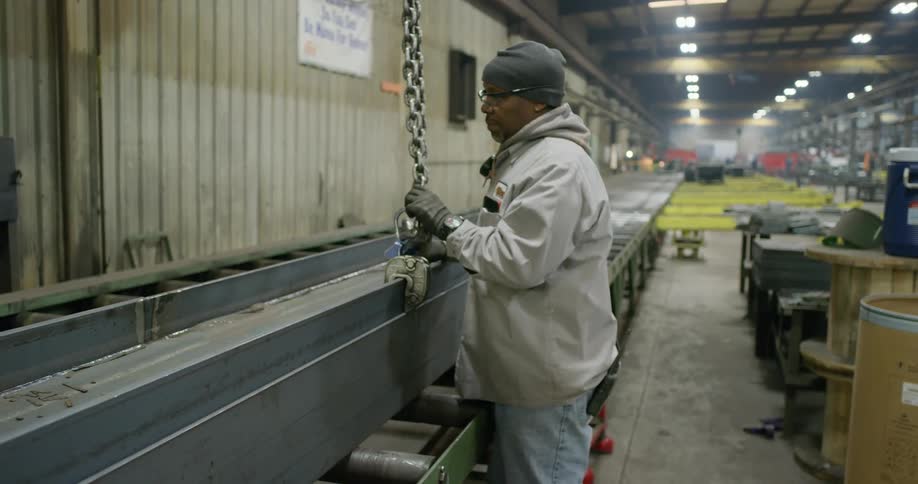 A man disconnects a chain clamp from a beam on a roller conveyor