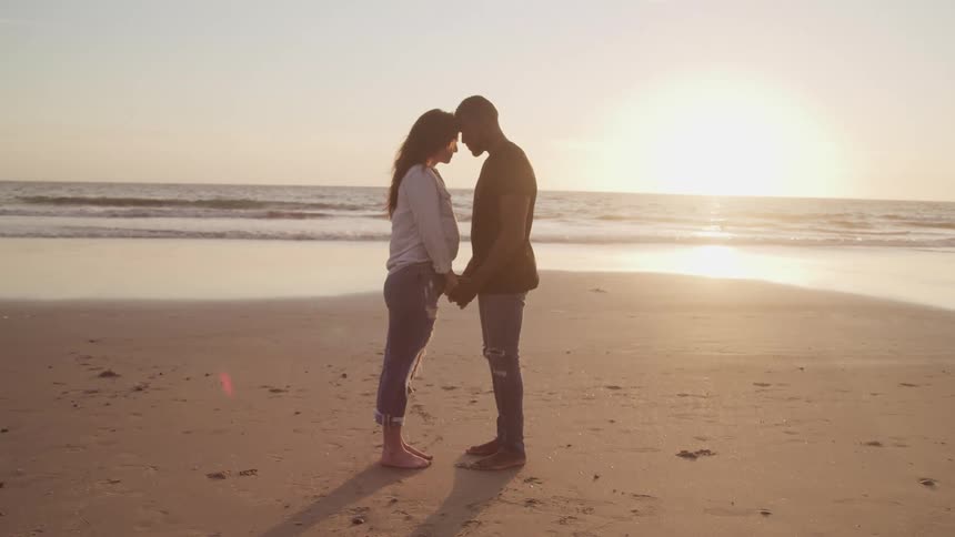 Couple lean close touching foreheads and holding hands on sunny beach