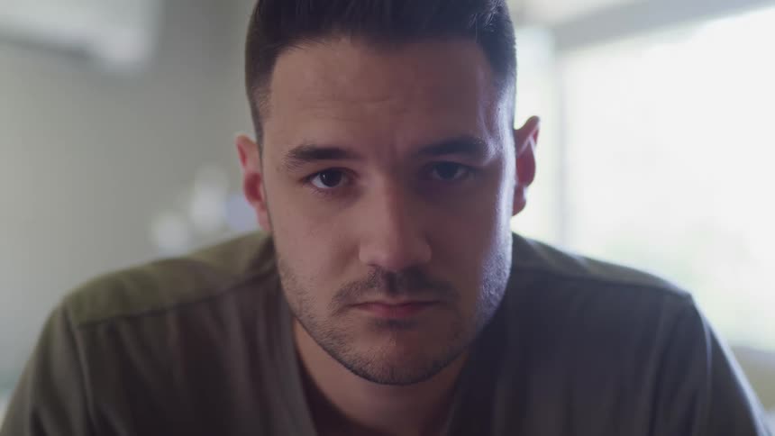 Man sitting in a room with white walls looks up at the camera