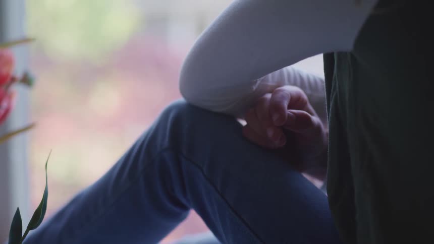 A person legs and arms while sitting on the ledge of a window looking outside