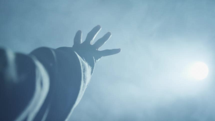 A person holds a hand towards a strobing light source in a smoky room