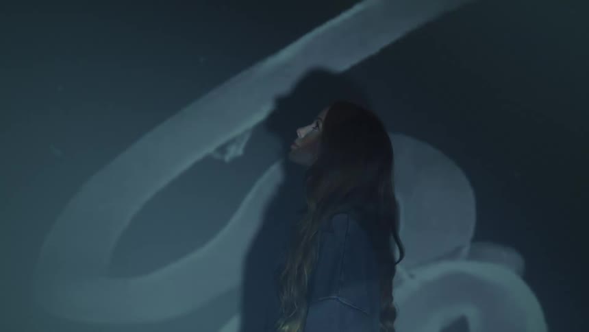 Film projecting over a young long haired woman standing in front of a white wall