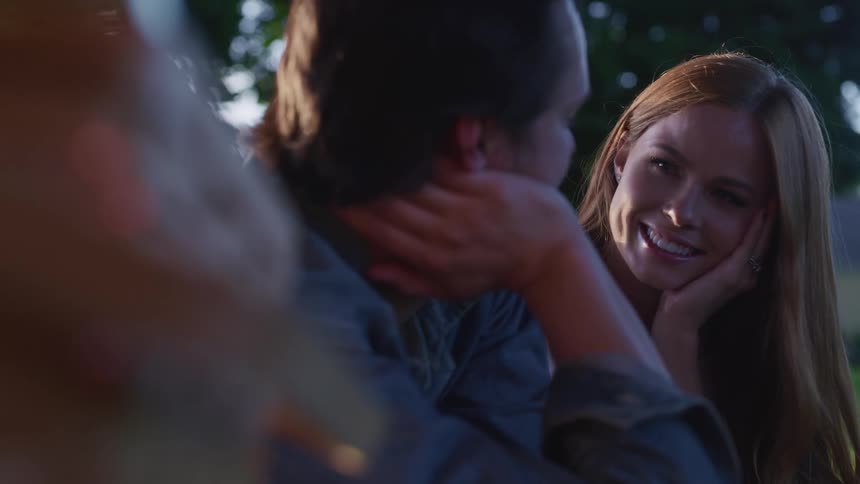 A man and woman outside rest their heads in their hands and look at one another as they talk