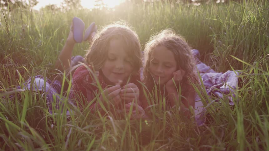 A boy and girl sit outside playing with blades of grass