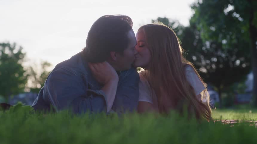 A man and woman laying in a park together and kissing
