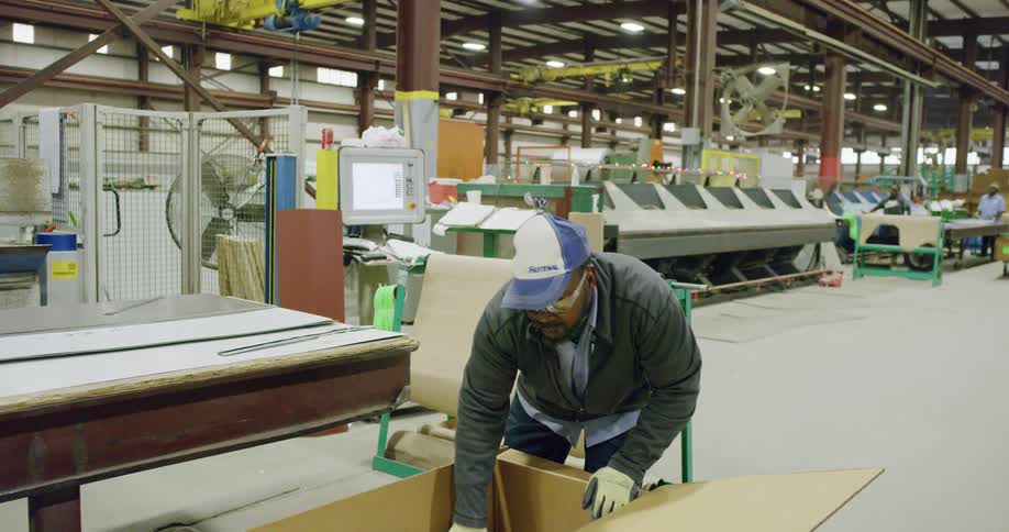 Worker places metal sheets inside a cardboard box in a factory inside a warehouse