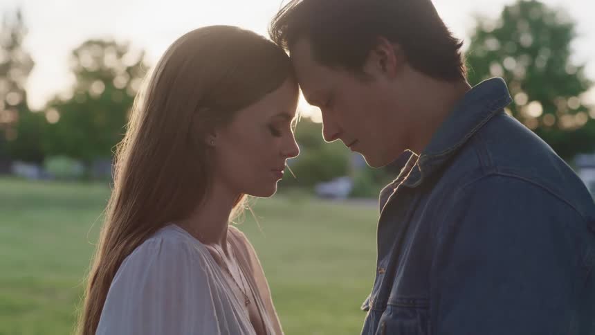 Man and woman romantically touch their heads together while standing in a field of green grass