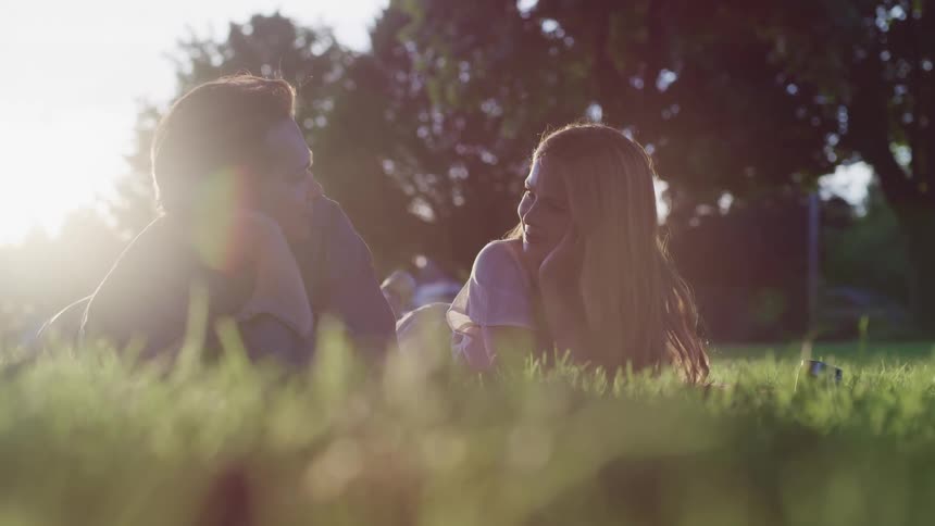 A man and woman laying and talking together in a park