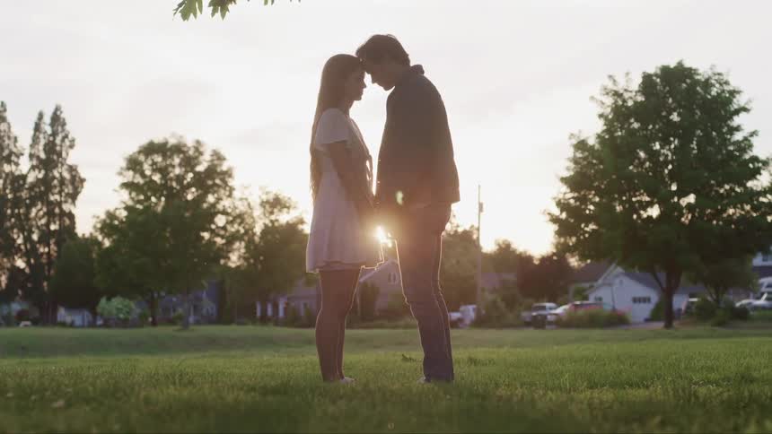 A man and woman hold hands and look in to one anothers eyes in a park in a neighborhood