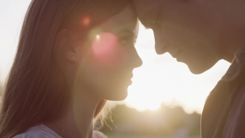 Man and woman touch their foreheads together romantically as they stand outdoors in the sun