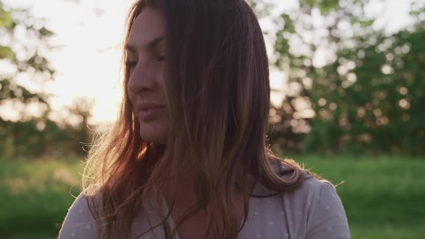 Close up of a long haired woman turning to look at the camera in a grass field at sunset
