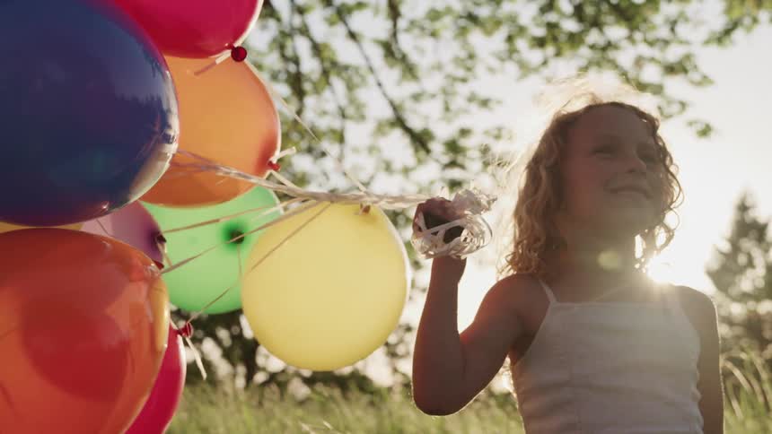 A girl is standing in the grass holding a bunch of balloons