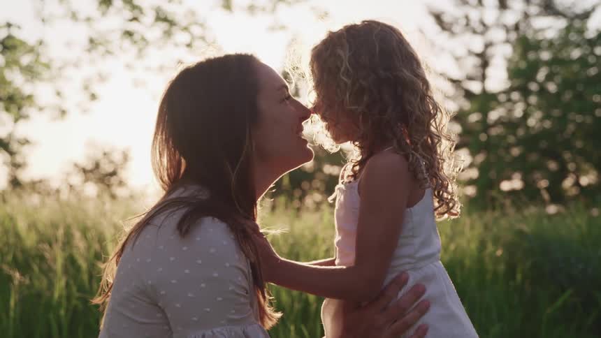Mother and daughter playing together touching their noses in the middle of a grass field