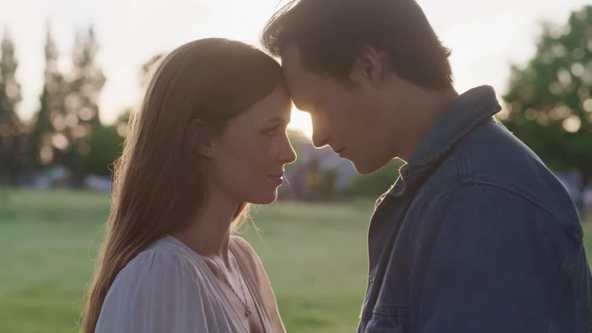 Young couple touching foreheads standing in a grass field at sunset