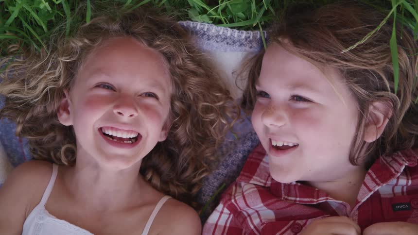 Two kids laying in the grass talking to each other and laughing