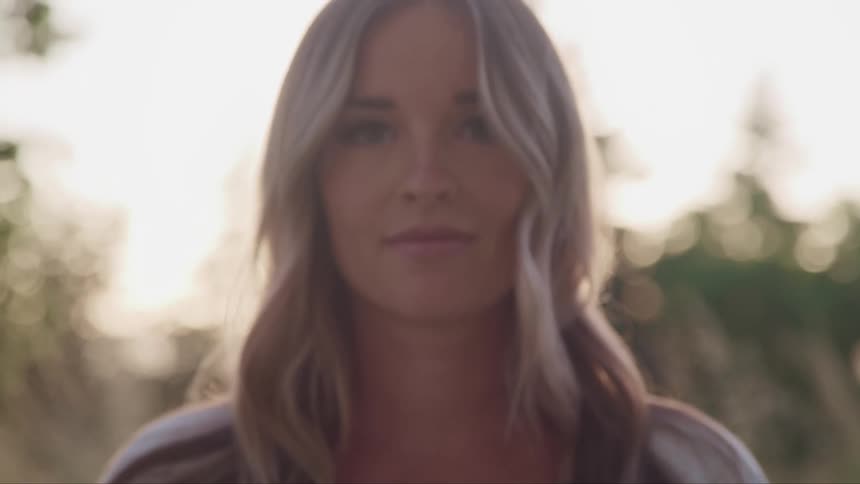 Young blonde woman looks up to the camera standing outdoors at sunset
