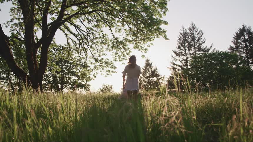 Mother and daughter spinning around in a green tall grass field at sunset