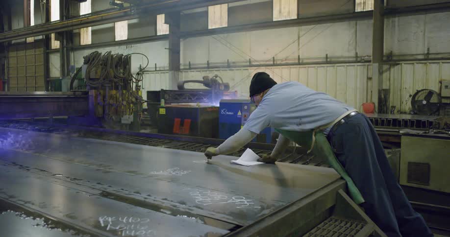 Workers marking and soldering sheets of metal on a factory inside a warehouse