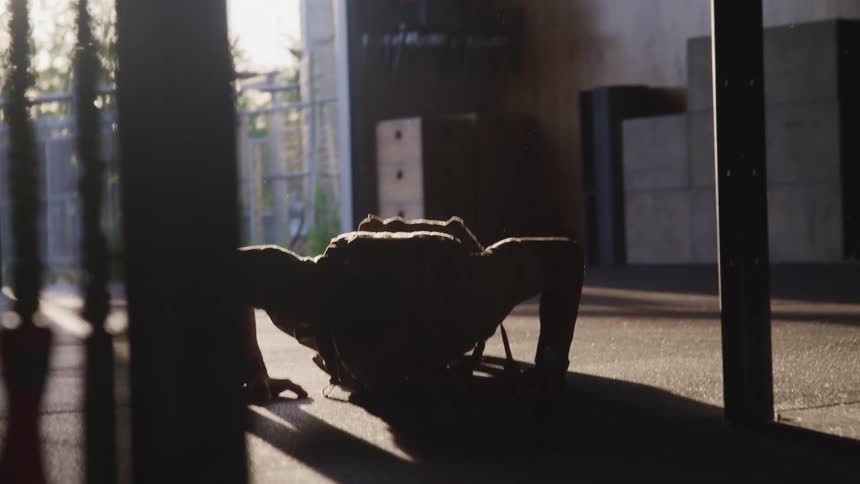Man doing push ups inside of a room with a large opening as the sun peers down on him