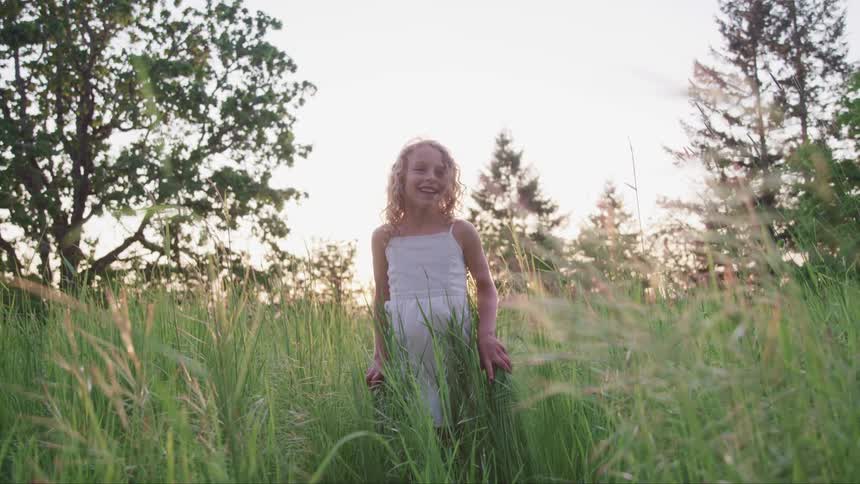 A young girl smiles and laughs as she stands in field of tall grass