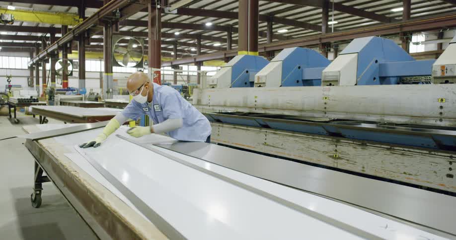 Worker assembling metal sheets out of a machine in a factory inside a warehouse