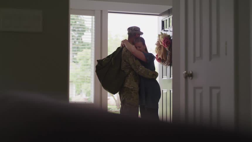 Military man and white woman hugging next to a door inside the house