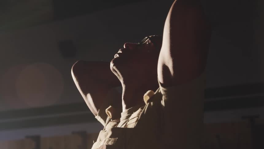 Tired man stretches his hands over the head inside a dimly lit room