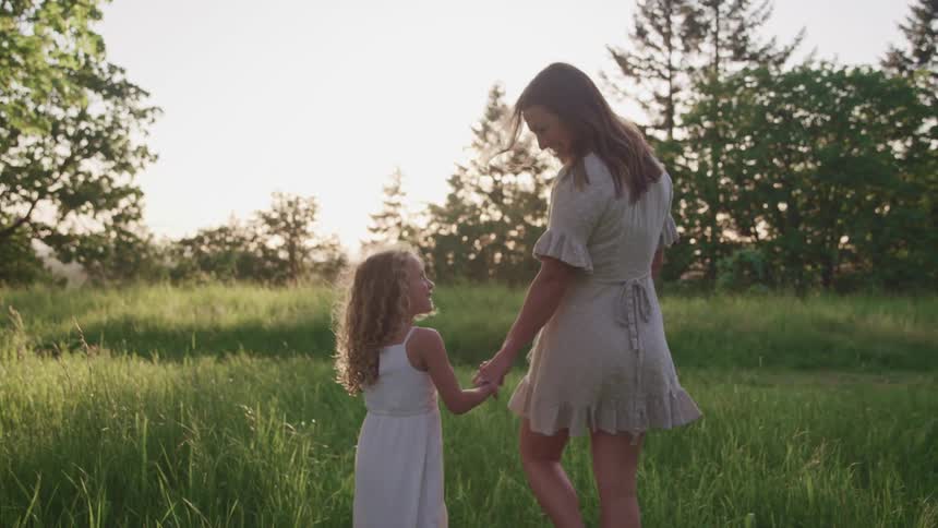 A mother and daughter holding hands and smiling at each other as they walk through the grass