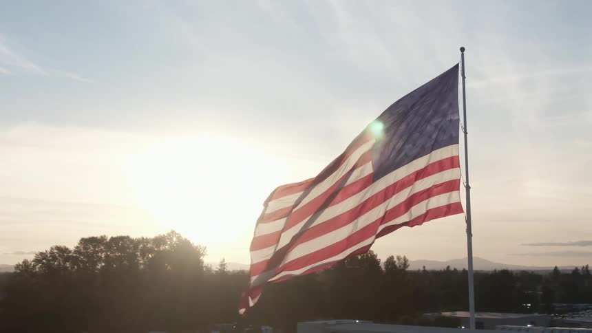 An american flag atop a flag pole waves as it looms over the surrounding countryside and buildings