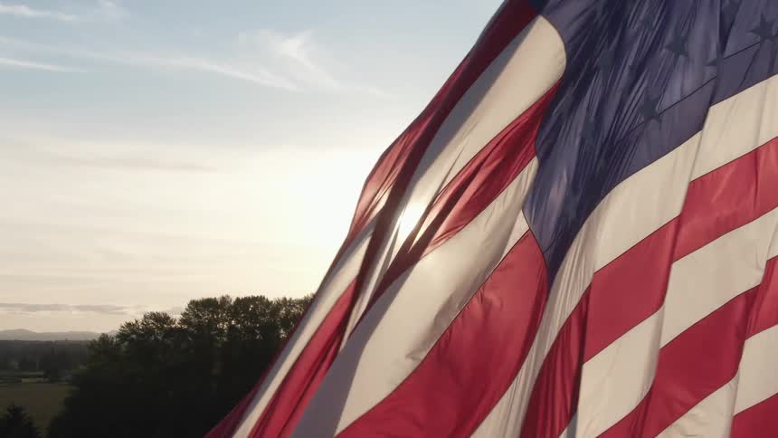 Sun flares behind an american flag flowing in the wind at daytime