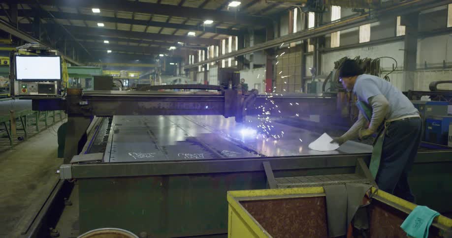 Sparks fly by a man as he marks sheet metal being cut in a factory