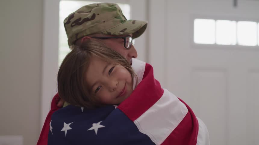 A young girl wrapped in a solider hugs her father who is dressed in a military uniform