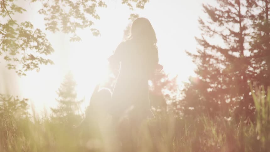 A mother swings her daughter around in a field and they laugh