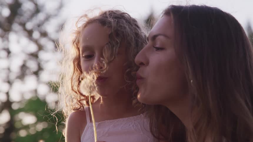 A woman and child blowing out a dandelion and smiling and laughing at eat other