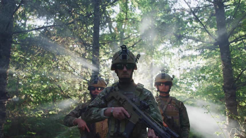 Soldiers wearing green camouflage holding assault rifles in the forest at morning