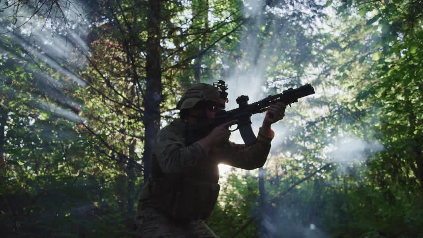 Soldier pointing a gun on the fog in the forest at sunset