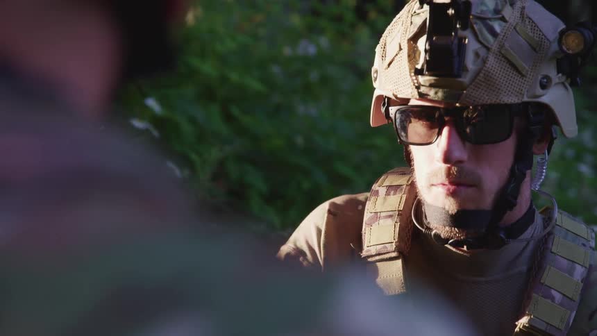 A man wearing tactical gear and holding a weapon face to face with another