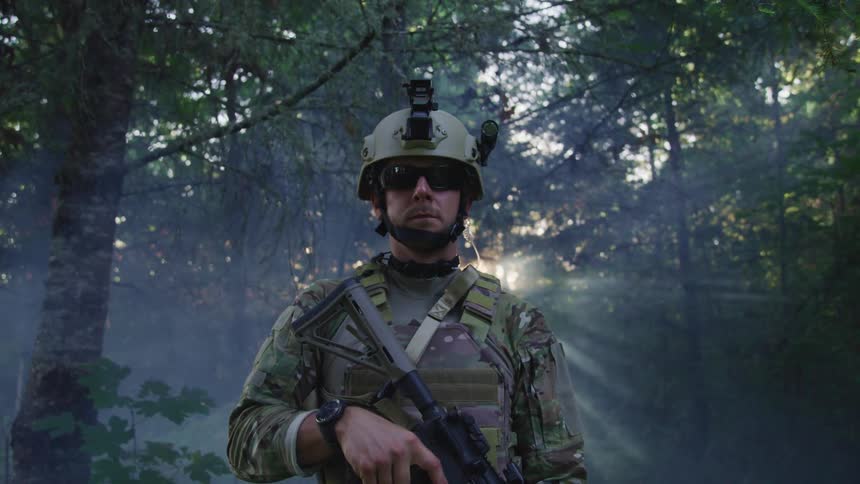 Soldier in combat gear standing in a forest at sunset
