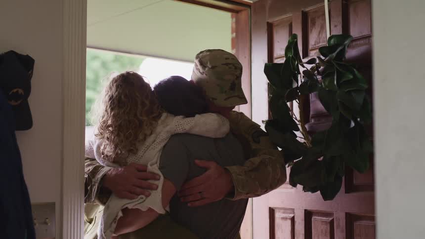 A soldier hugs his wife and daughter at the front door of their home