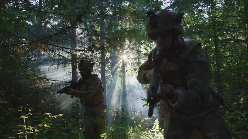 Military men holding guns and walking together in the middle of a forest