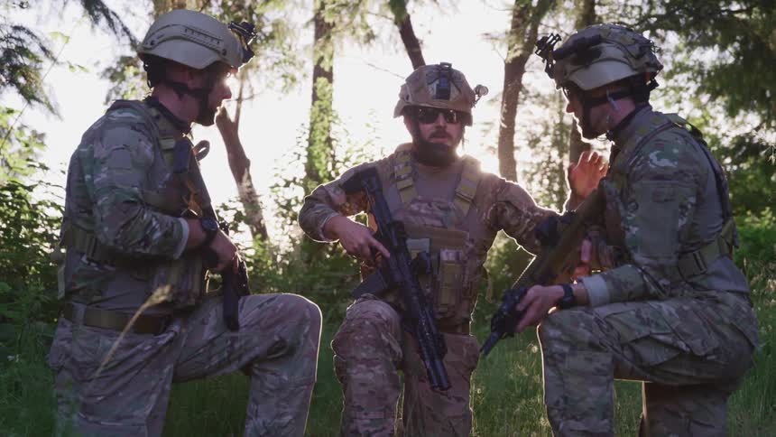 Soldiers crouched together and talking to each other in the middle of a forest