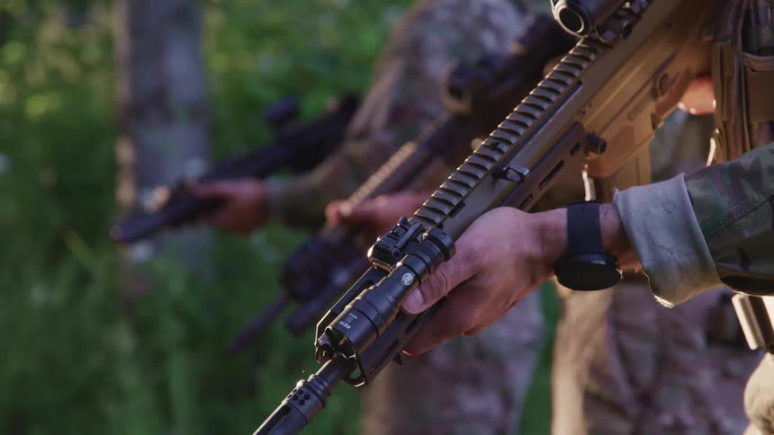 Three soldiers holding assault weapons standing in the forest at evening