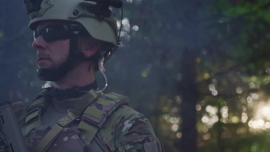 Sun shines through trees behind soldier wearing combat gear