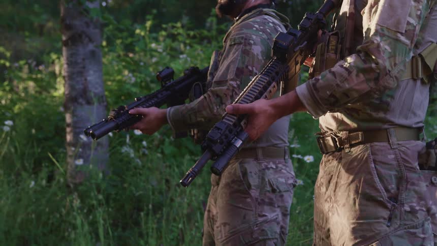 Three men standing and holding rifles with trees and plants in the background