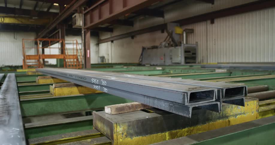 Narrow steel panels are lined across a table in a factory