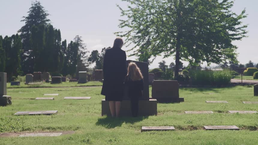 A woman and child standing in front of a gravestone in a cemetery