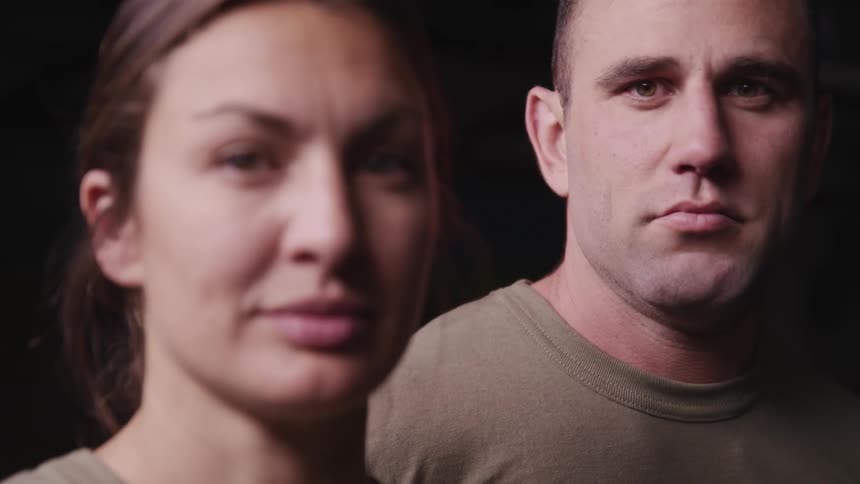 A man and a woman stand looking at the camera in matching shirts