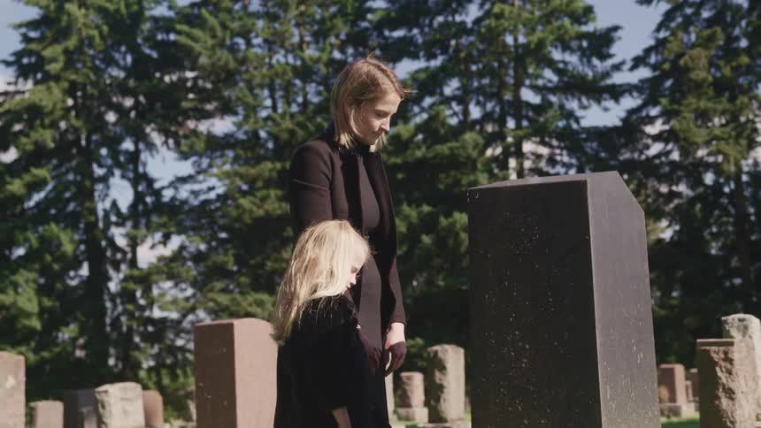 A woman and girl stand in front of a gravestone during the day