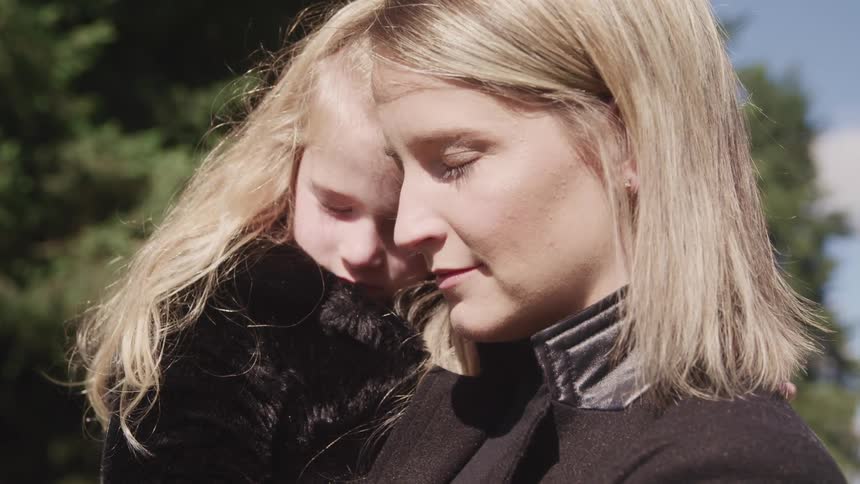 Mother holding daughter in her arms pensively outdoors